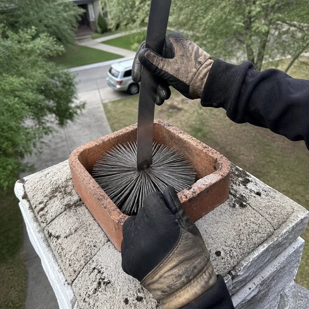 Professional technician performing a chimney sweep with a wire brush.